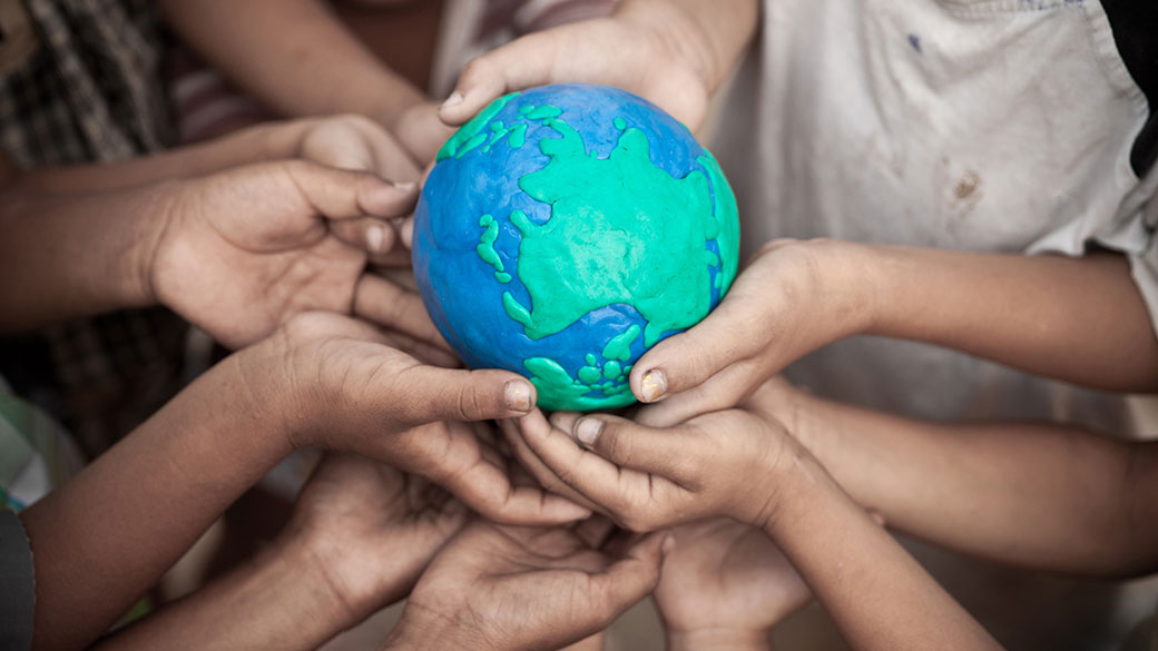 Group of children's hands holding up a small globe made of clay.