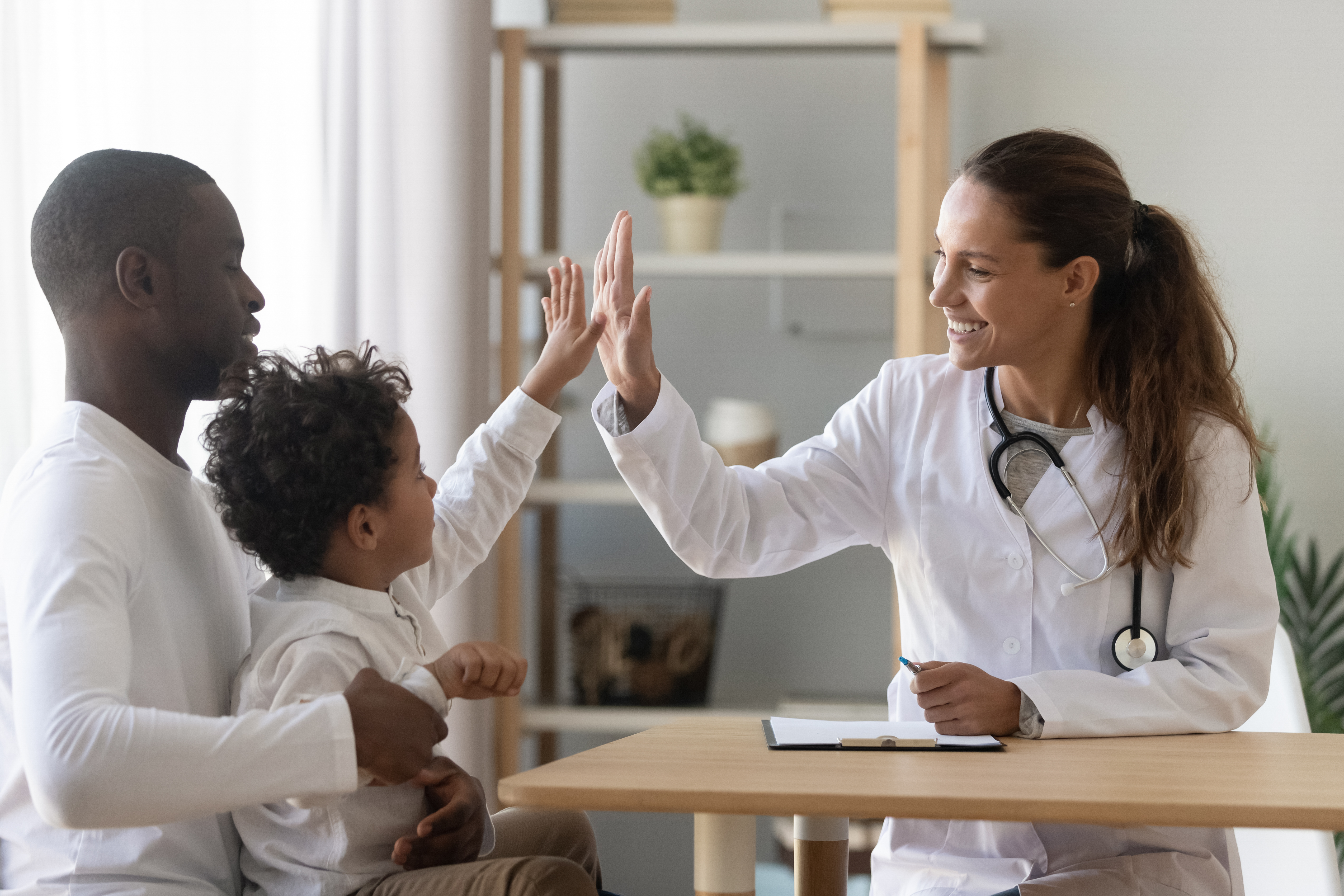 Child on father's lap giving a high five to a pediatrician.