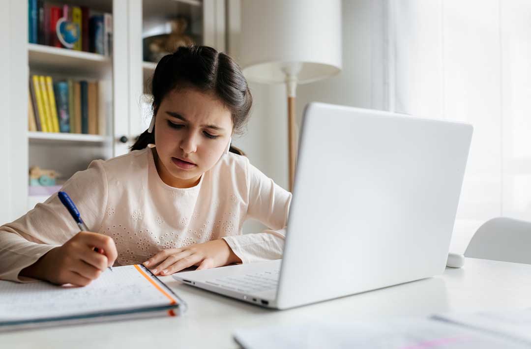 Girl struggling with remote schooling with laptop and notebook.